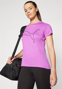 Camiseta de manga corta morada con un logo negro de Puma en el frente; combinada con leggings negros y una bolsa de deporte negra.