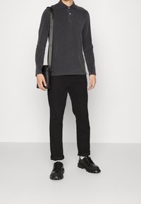 Tmavě šedá polo košile s dlouhým rukávem a límcem, spárovaná s černými kalhotami a černými botami. Má minimalistický design a ramenní tašku.