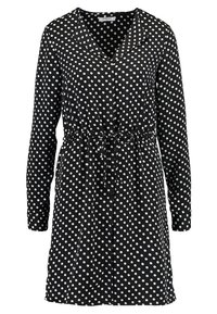 Svart klänning med långa ärmar, vita prickar, v-ringning, rynkad midja med snörning och en avslappnad passform. Tillverkad av lättviktsmaterial.