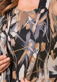 Langarm blouse in zwart, beige en grijs met abstracte patronen. Zachte stof, ronde hals en een loose fit met opvallende penseelstreekdetails.