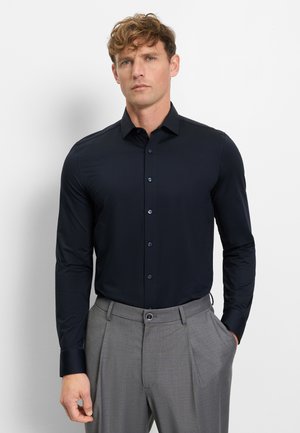 Marineblaues Langarmhemd mit Knopfkragen und kontrastierenden Manschetten. Glatter Stoff, kombiniert mit grauen plissierten Hosen.