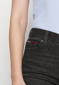 Svarta denimjeans har en smal passform med vita sömmar och en liten röd, vit och blå logoprydnad på framfickan.