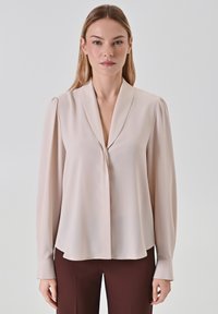 Helle beige Bluse mit Schalkragen, langen Ärmeln und glatter Textur. Verfügt über einen dezenten Fall und eine frontale Verschluss.