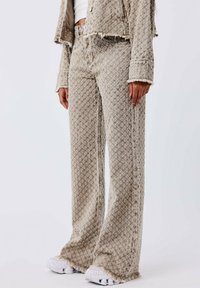 Jeans de pierna ancha de color beige con un acabado texturizado, que presentan bordes deshilachados y un ajuste relajado, combinados con zapatillas blancas.