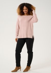 Ljust rosa stickad tröja med lång ärm och bred rund halsringning, matchad med tighta svarta byxor och tanfärgade ankelstövlar.