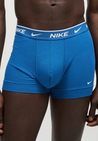 Αρσενικός κορμός που φοράει μπλε boxer της Nike με χαρακτηριστική μέση και λογότυπο swoosh στο αριστερό μηρό σε απλό φόντο.