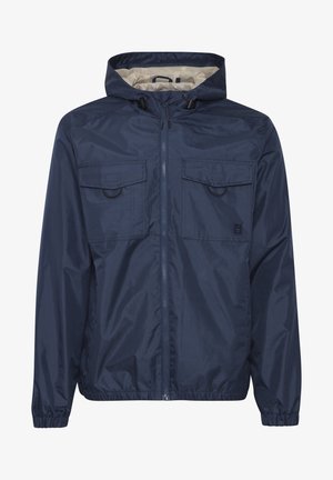 Námornícky modrý windbreaker s kapucňou, plným zipsom, dvoma náprsními vreckami, elastickými manžetami a vnútorným podšívkou v kontrastnej svetlej farbe.