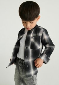 Sort og hvid plaid skjorte med lange ærmer og en lomme, parret med lys grå denim jeans. Glat stofstruktur.