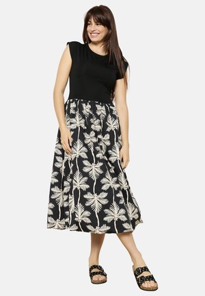 Black dress with a short sleeve top and a flowy skirt featuring white palm tree patterns. Model wears open-toe black sandals.