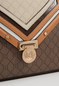 Gros plan sur le coin d'un sac à main multi-tons en cuir marron, beige et fauve, avec des garnitures en métal doré et une base en tissu à motif.