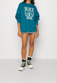 Teal Nike-tröja med vitt logo, matchad med en svart-och-vit rutmönstrad minikjol. Svarta höga stövlar med vita sulor.