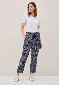Pantaloni blu navy con motivo a foglie bianche, vita elastica, due tasche laterali e una vestibilità rilassata, abbinati a una maglietta bianca semplice e sneakers bianche.