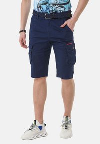 Marine cargoshorts met meerdere zakken, riemlussen, versterkte naden en een gladde textuur. Gekocht met witte sportschoenen.