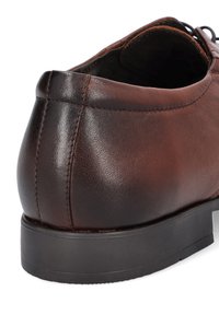 Brązowy skórzany but o gładkiej fakturze, zaokrąglonym obcasie i subtelnych detalach przeszycia. Gumowa podeszwa o niskim profilu zapewniająca stabilność.