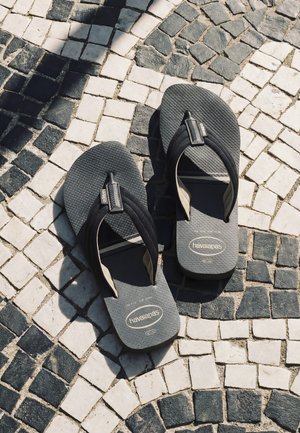 Tongs noires Havaianas posées sur un pavement en mosaïque blanc et noir avec la lumière du soleil et des ombres alentours.