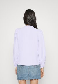 Pullover lilla con maniche a sbuffo, realizzato in tessuto morbido. Abbinato a una mini gonna di jeans con orlo sfilacciato e tasche posteriori.