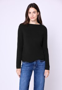 Czarny sweter z dzianiny z szerokim dekoltem i długimi rękawami, w połączeniu z niebieskimi dżinsami. Miękka faktura, luźny krój i prosty design.