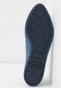 Semelle de chaussure tricotée bleue avec du caoutchouc noir texturé. Présente un motif de lignes courbes et le nom de la marque "Skechers" embossé sur le côté.