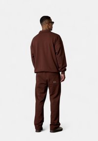 Sweatshirt marron avec une coupe décontractée et un col, assorti à un pantalon de jogging avec un petit logo sur la poche arrière.