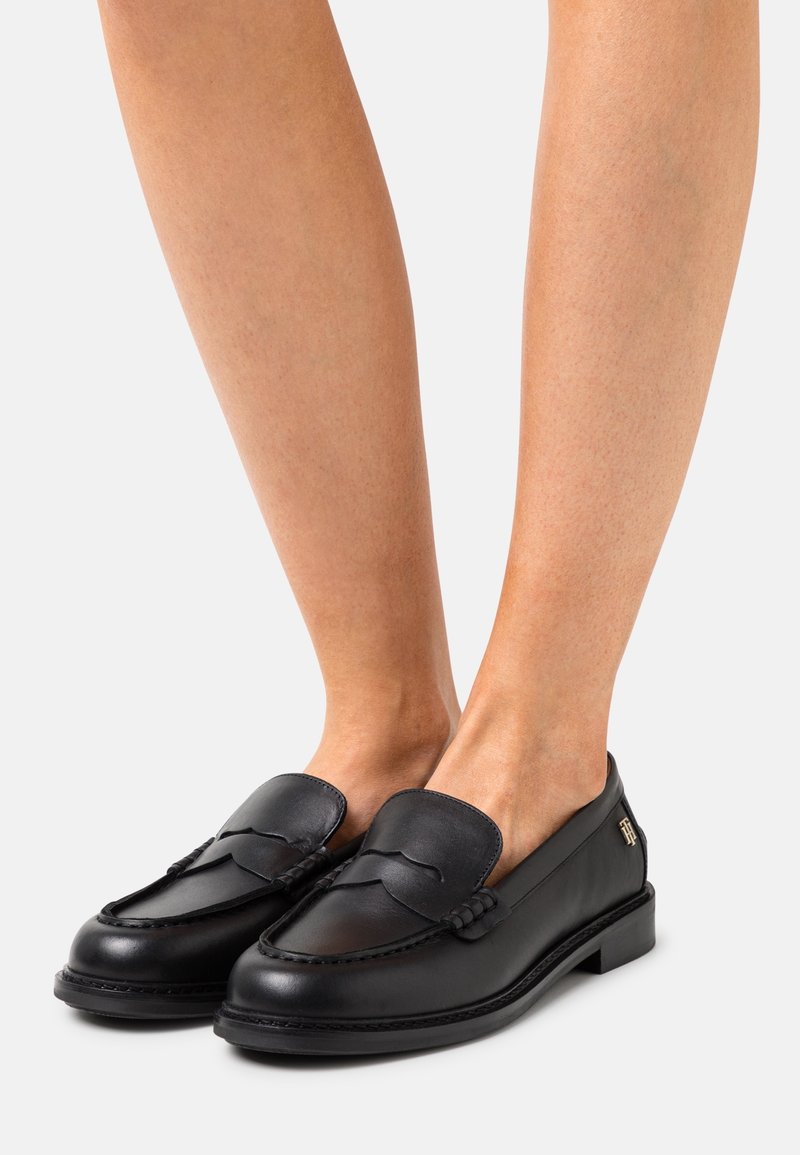 Mustat nahkaiset loafersit matalalla korolla, joissa on ommeltu muotoilu, sileä pinta ja koristeellinen yksityiskohta sivussa.