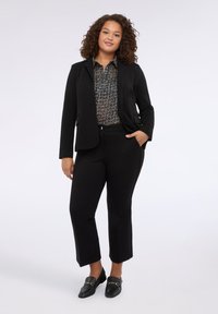 Černý blazer přes vzorovanou černobílou blůzu, doplněný černými zkrácenými kalhotami a nazouvacími botami se zlatými akcenty.