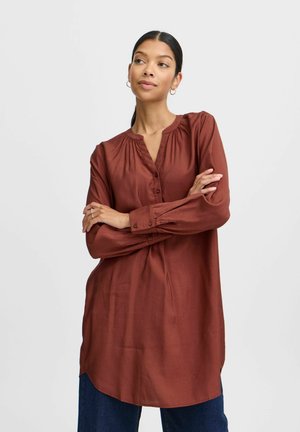 Blouse à manches longues de couleur rouille en tissu lisse, avec un col rond, une fermeture par boutons et des détails de plissés sur le devant.