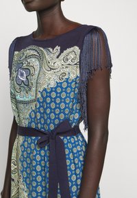 Robe composée d'un haut bleu marine avec des détails à franges, d'une jupe bleue à motifs cachemire et pois, et d'une ceinture assortie en tissu.