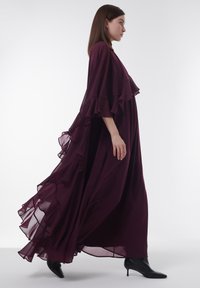 Maxikleid aus tiefburgunderfarbenem Chiffon mit gestuften Rüschendetails an den Ärmeln und dem Saum. Hat eine legere Passform und einen subtilen Glanz.