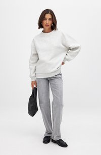 Lichtgrijze sweatshirt van een zachte stof, gecombineerd met lichtgrijze rechte spijkerbroek en een zwarte geweven tas. Zwarte instapschoenen maken de outfit compleet.
