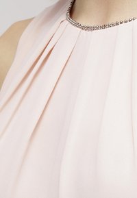 Vaaleanpunainen hihaton paita, jossa on poimutuksia ja koristeelliset hopeiset helminäytön kaula-aukko. Sileä kangas, jossa on pehmeä rakenne.