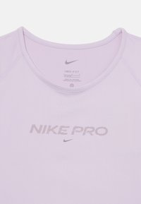 Svijetlo ljubičasta Nike Pro majica s okruglim izrezom. Izrađena od Dri-FIT materijala. Ima sivi logo i natpis sprijeda. Mekana, glatka tekstura.
