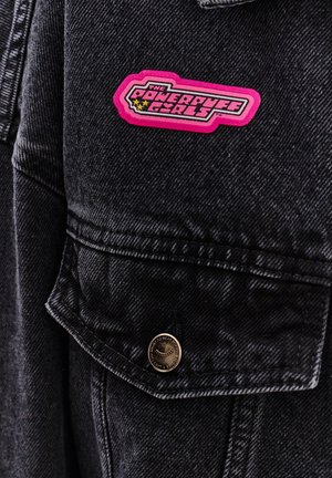 Czarna kurtka dżinsowa z wyraźną różową naszywką z logo "Powerpuff Girls" na kieszeni piersiowej oraz z mosiężnymi zatrzaskami.