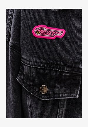 Czarna kurtka dżinsowa z wyraźną różową naszywką z logo "Powerpuff Girls" na kieszeni piersiowej oraz z mosiężnymi zatrzaskami.