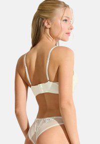 Kant bralette in licht crèmekleur met verstelbare bandjes en haak-en-oogsluiting; bijpassende sheer thong met bloemenborduursel en zachte mesh.