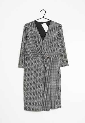 Robe portefeuille à motifs noir et blanc, longueur genou, avec manches trois-quarts, suspendue sur un cintre noir contre un fond blanc.