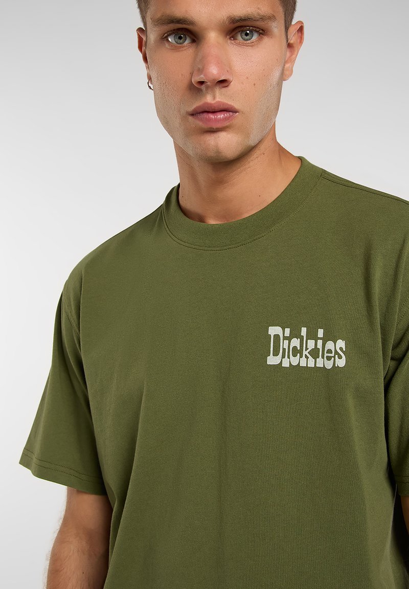 T-shirt à manches courtes vert olive en coton, avec un logo blanc imprimé sur le côté gauche de la poitrine. Encolure ronde, coupe standard.