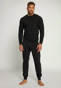 Sudadera negra con patrón de puntos blancos, de mangas largas y cuello redondo, combinada con pantalones jogger negros con puños elásticos.