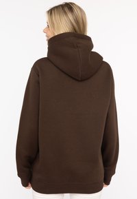Brązowy sweatshirt z kapturem o luźnym kroju, z prążkowanymi mankietami i dołem. Gładka tekstura z wyraźnym szczegółem kaptura.