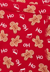 Červená látka s opakujícím se motivem perníčků s úsměvem a nápisem „Ho“ spolu s malými sobími čepicemi. Měkký, pružný materiál.
