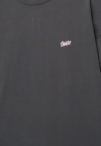 Sweatshirt gris foncé à col rond avec un petit texte brodé rose "SNYP." sur le côté gauche de la poitrine.