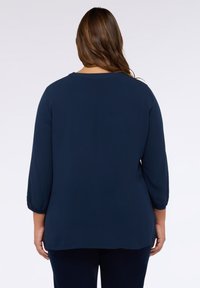 Marineblauwe blouse met driekwart mouwen en een ronde halslijn. Gemaakt van een gladde stof, met gerimpelde details aan de mouwen.