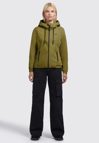 Olive green lightweight jacket with a drawstring hood, front zip closure, and elastic cuffs. Paired with black cargo pants featuring multiple pockets.