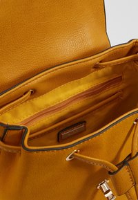 Wnętrze żółtej skórzanej torebki z teksturowanym wykończeniem, wyposażone w kieszeń na zamek oraz gładką podszewkę z tkaniny. Detale obejmują złote okucia.