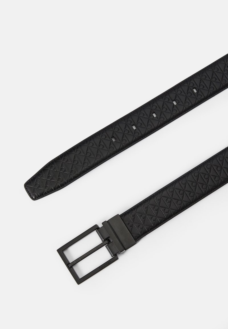 Sort tekstureret læderbælte med et geometrisk mønster, sølv rektangulær spænde og flere justeringshuller langs remmen.