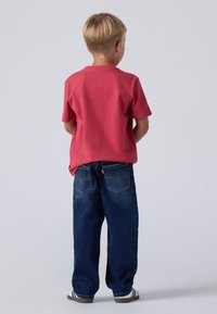 Camiseta de algodón roja de manga corta combinada con unos vaqueros de denim azul sueltos. Los vaqueros tienen bolsillos traseros y detalles de costura sutiles.