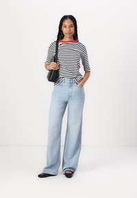 Gestreiftes schwarz-weißes Oberteil mit rotem Kragen, kombiniert mit hellblauen Weitbeinjeans. Eine schwarze Handtasche und schwarze Ballerinas runden das Outfit ab.
