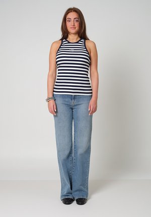 Gestreept mouwloos topje in marineblauw en wit, gecombineerd met lichtblauwe flared jeans, gedragen met zwarte schoenen. Eenvoudig ontwerp en relaxte pasvorm.