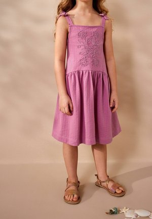 Rosa Baumwollkleid mit besticktem Blumenmuster, quadratischem Ausschnitt und Schulterbindebändern. Ausgestellter Rock und kombiniert mit hellbraunen Riemchensandalen.