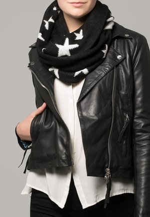 Personne portant une veste en cuir noire sur une chemise blanche et une écharpe noire à motifs d'étoiles blanches, main dans la poche de la veste.