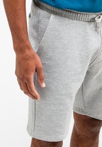 Grijze katoenen shorts in een blend met een elastische tailleband, zijzakken en een soepele textuur, gedragen door een persoon met een hand die ernaast rust.